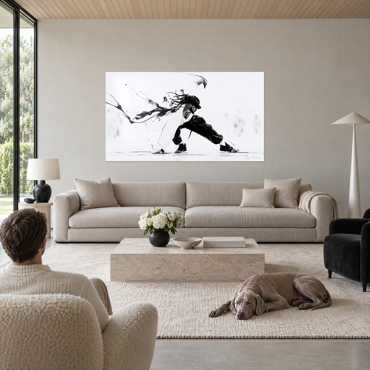 Wall art of a breakdancer slicing through space, black cap and strands on a white background, two people seen from behind and a Weimaraner above a sofa in a bright living room