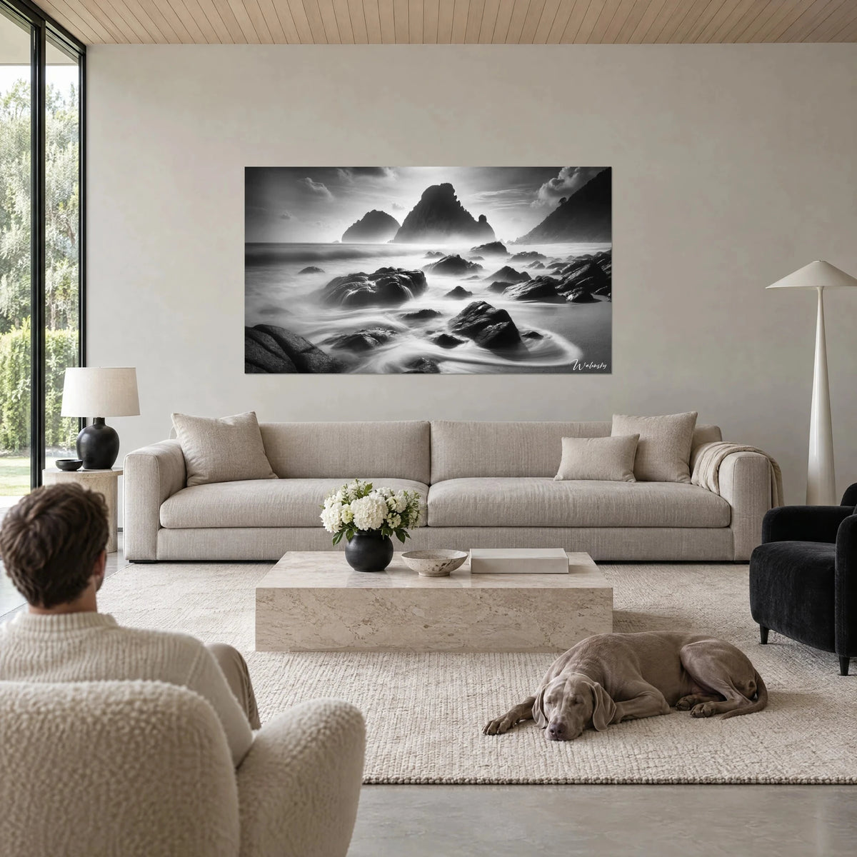 Tableau pics rocheux noyés de brume sur une mer lisse, gris perle et noir profond, au-dessus d'un canapé dans un salon lumineux