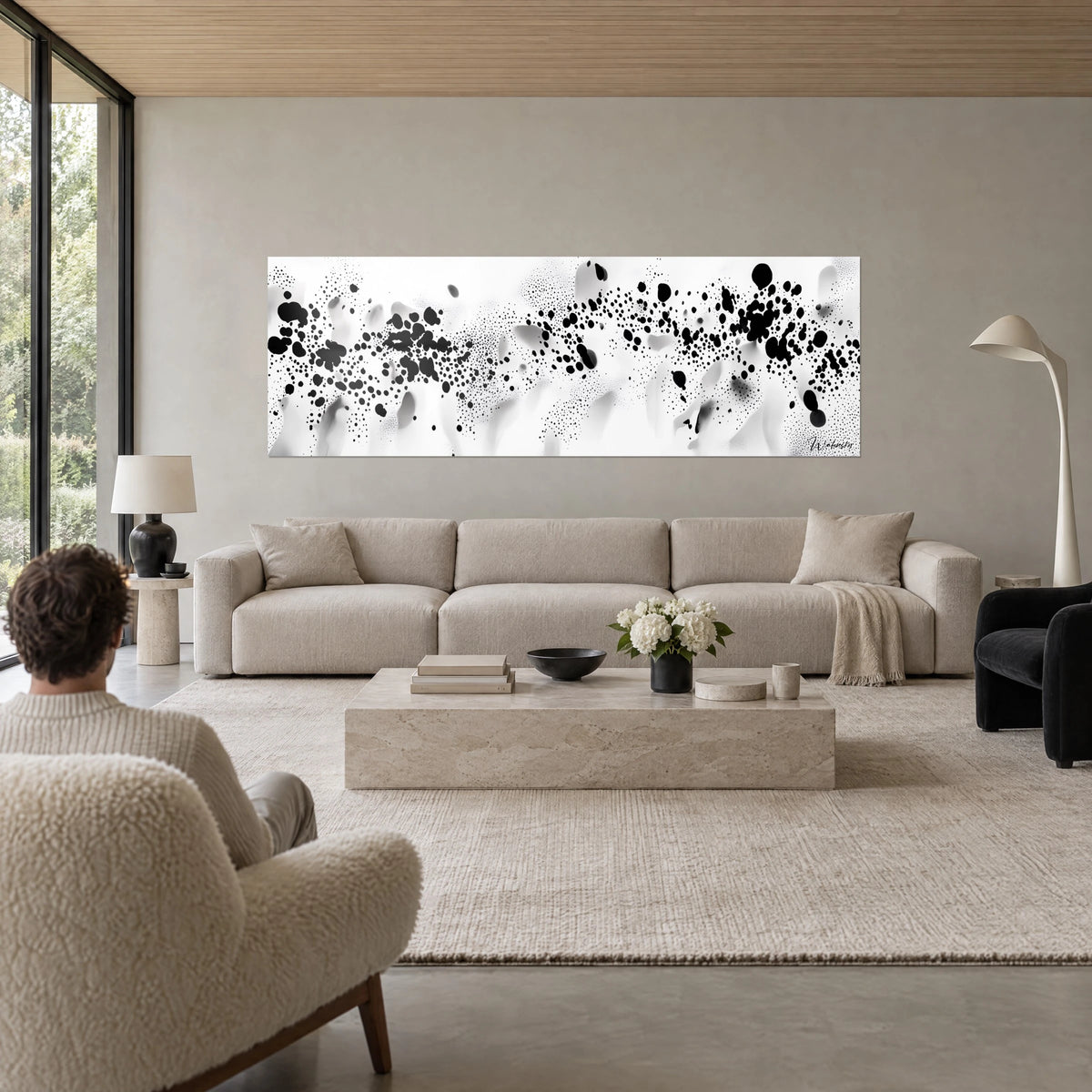 Schilderij met zwarte inktspatten op een nevelig wit achtergrond, persoon van achteren, boven een bank in een lichte woonkamer