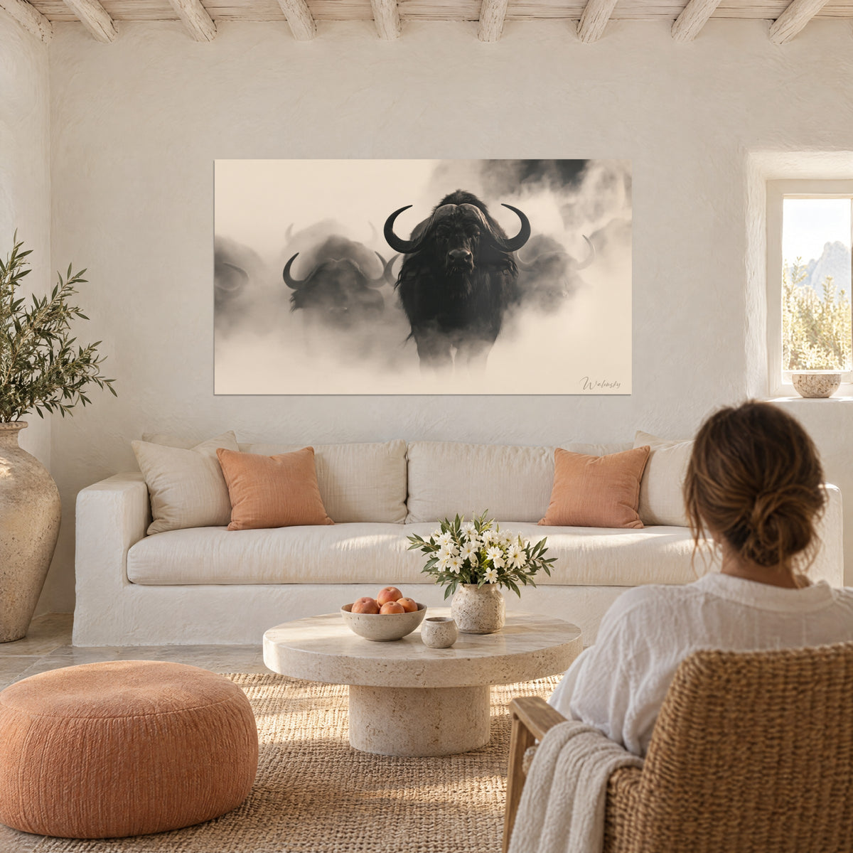 Tableau buffle noir aux cornes recourbées dans la brume beige, troupeau flou derrière, au-dessus d'un canapé dans un salon lumineux