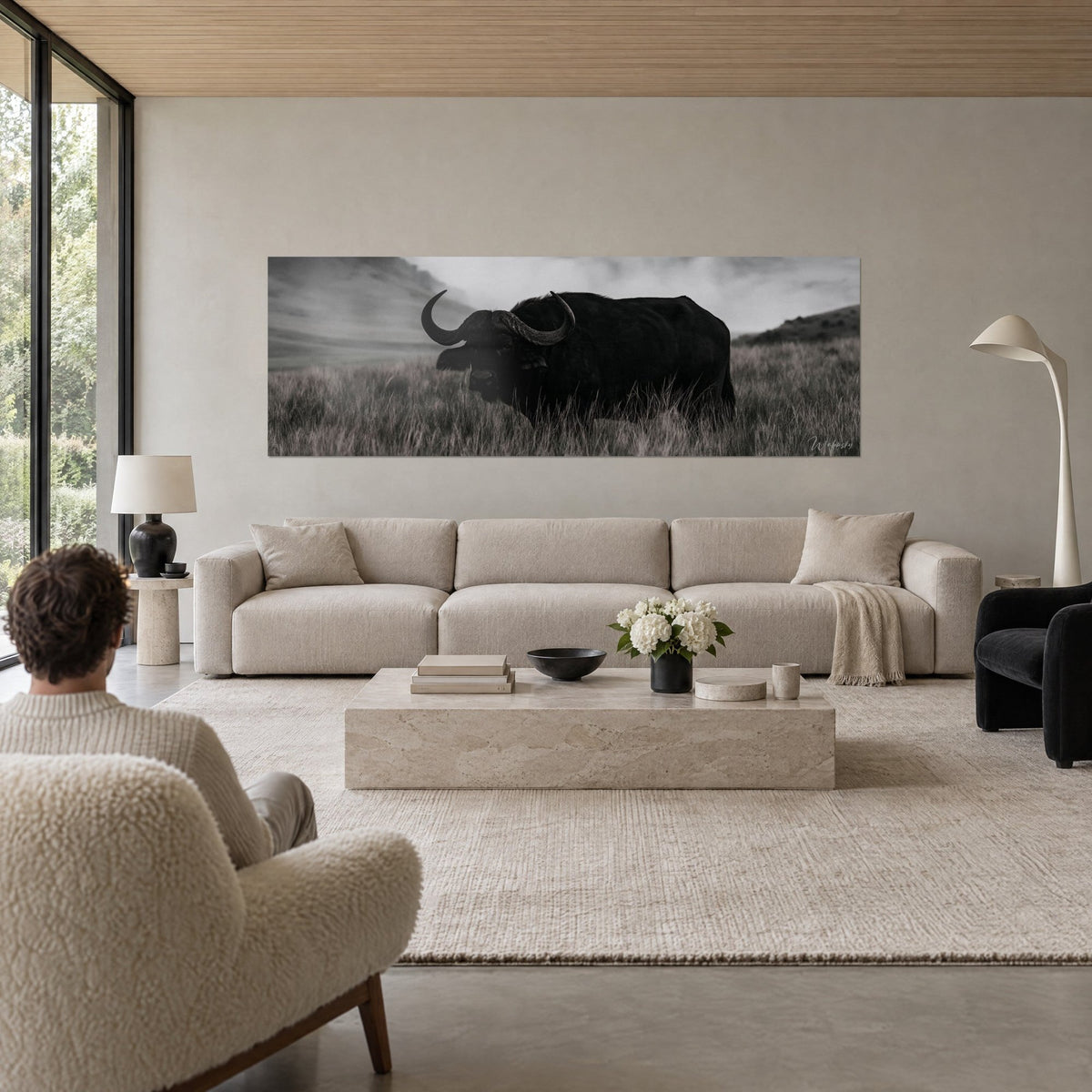 Quadro bufalo nero di profilo, corna ricurve nell'erba secca grigia, colline nebbiose, sopra un divano in un soggiorno luminoso