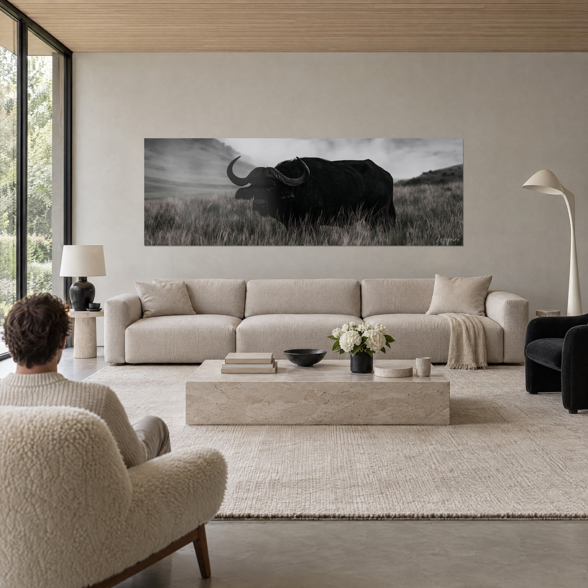 Quadro bufalo nero di profilo, corna ricurve nell'erba secca grigia, colline nebbiose, sopra un divano in un soggiorno luminoso