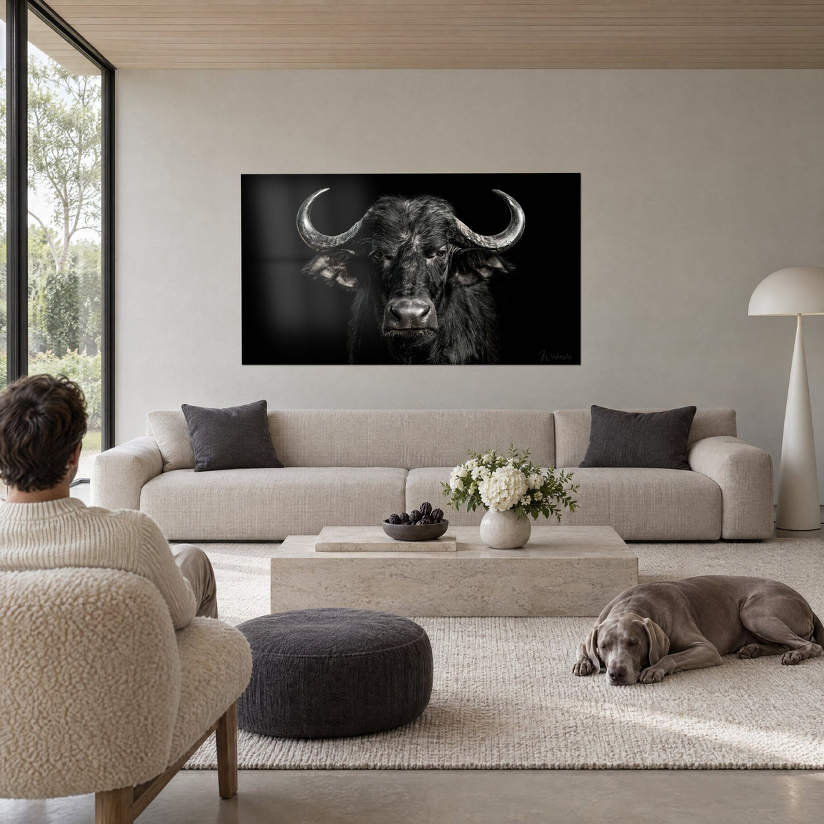 Schilderij zwarte buffel met zilverkleurige hoorns in halvemaanvorm, harig antracietkleurig vacht, boven een bank in een lichte woonkamer