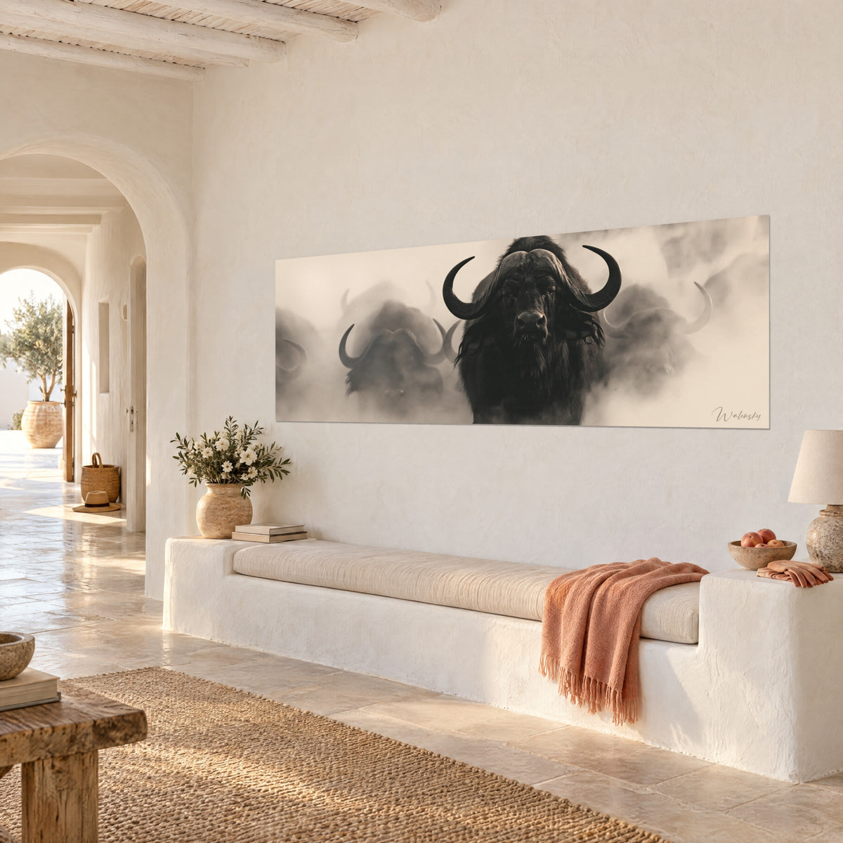 Wall art Dark African wild bull facing us head-on, blurred beige and grey herd behind, whitewashed wall, stone bench