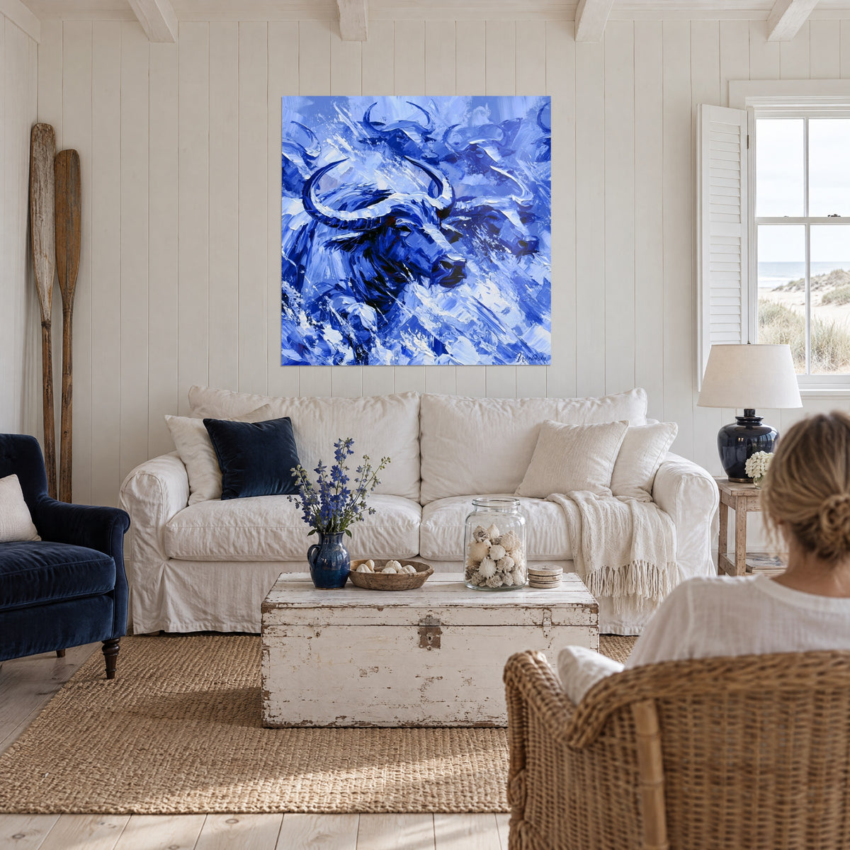 Wall art water buffalo with crescent-shaped horns, cobalt blue and cream white, thick palette-knife texture, above a sofa in a bright living room