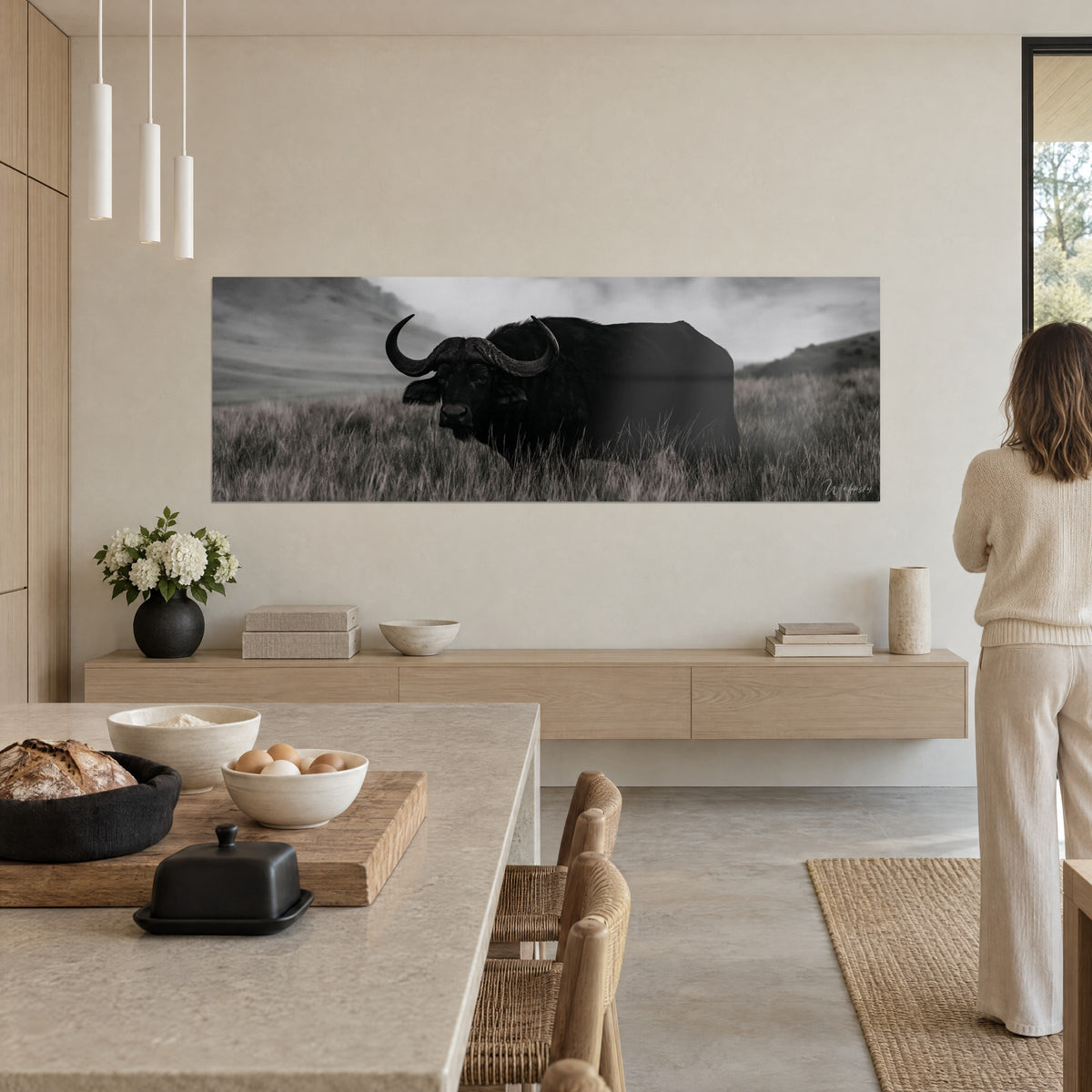 Schilderij gehoornd dier in zwart-wit tegen mistige heuvels, grijs gras, beige muur van een open keuken, vrouw van achteren