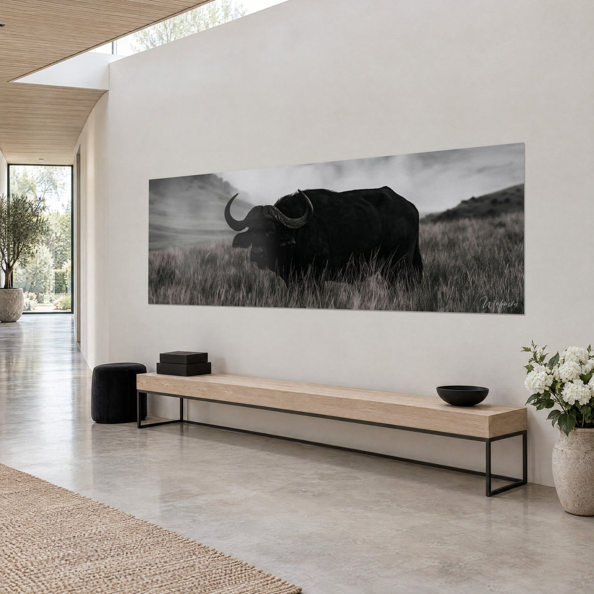 Quadro toro selvatico africano, manto nero carbone e cielo grigio velato, visto di tre quarti su una parete color crema, panca bassa in legno chiaro