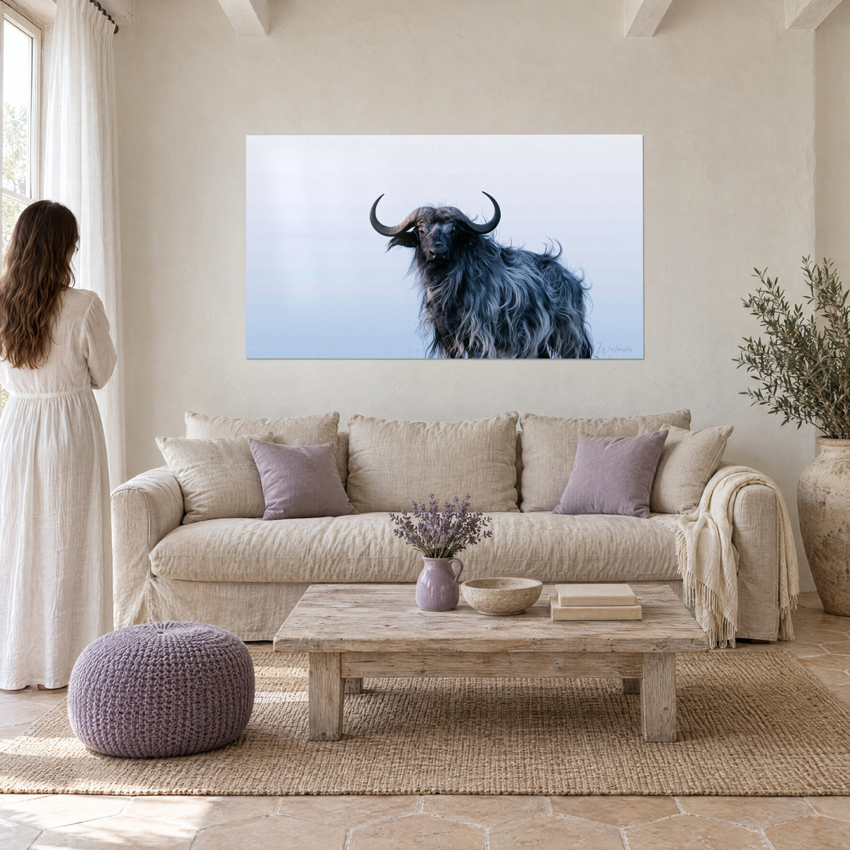 Tableau buffle sombre aux cornes recourbées, crinière grise ébouriffée sur ciel bleu pâle, au-dessus d'un canapé dans un salon lumineux