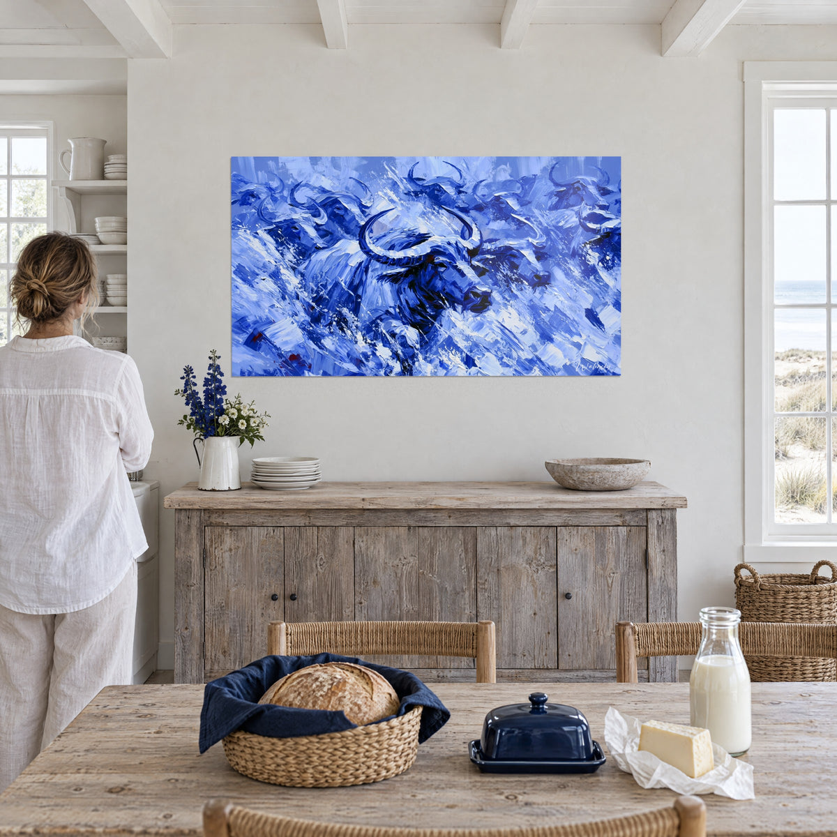 Wall art buffalo stampede in palette-knife painting, deep indigo and brilliant white, woman seen from behind, seaside house