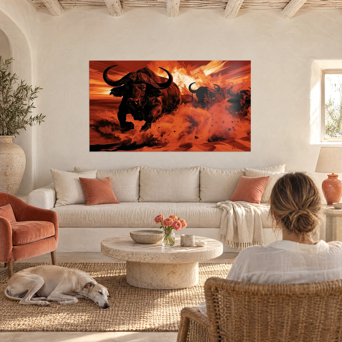 Wall art herd of black buffalo charging through ochre and red dust, above a sofa in a bright living room