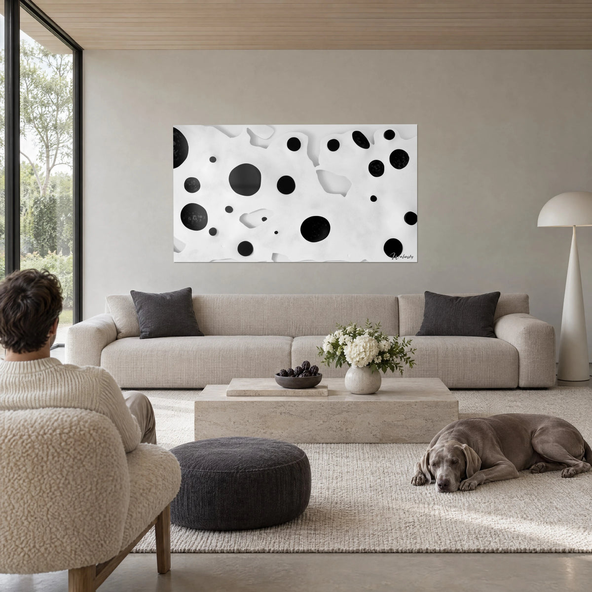 Wall art with black discs on cream white relief, two figures seen from behind and a grey Weimaraner, above a sofa in a bright living room
