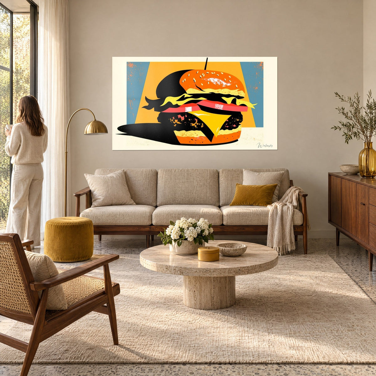 Tableau cheeseburger stylisé aux aplats orange et noirs, fond jaune moutarde, une femme de dos au-dessus d'un canapé dans un salon lumineux