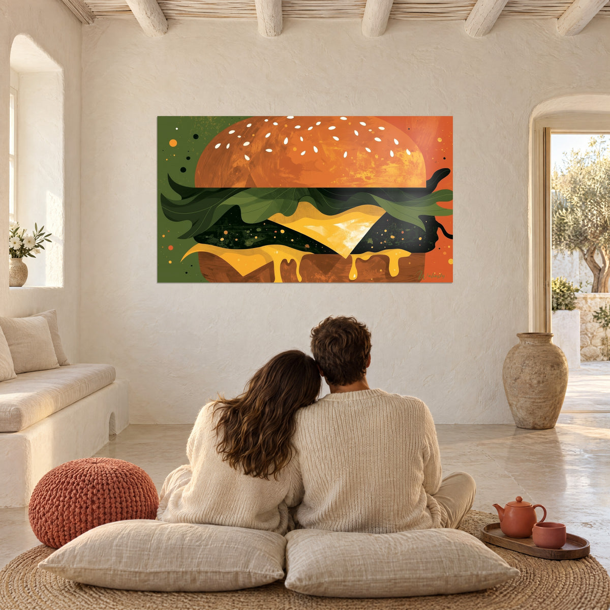 Πίνακας μπέργκερ pop-art, έντονο κίτρινο τυρί, πράσινη μούσα σαλάτα και κοκκινωπό ψωμί, κρεμασμένος πάνω από μαξιλάρια όπου κάθεται αγκαλιασμένο ζευγάρι