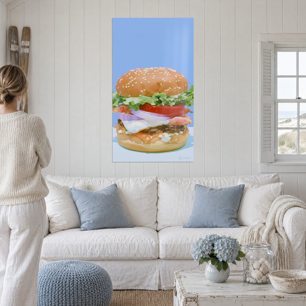 Tableau cheeseburger géant à l'œuf poché, pain doré sésame et fond bleu ciel, au-dessus d'un canapé dans un salon lumineux