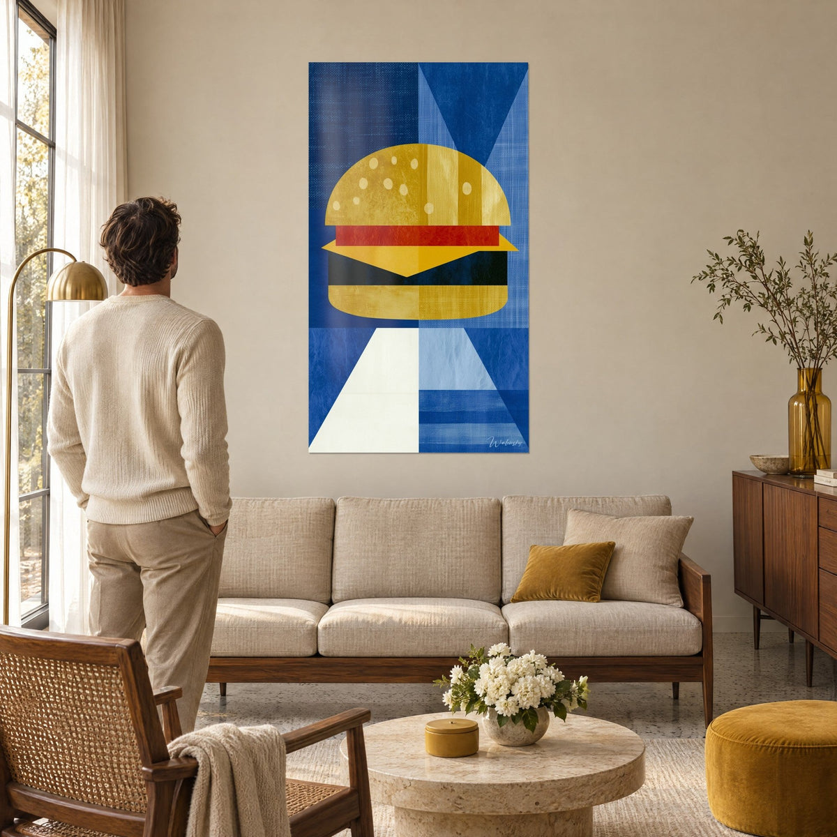Wall art geometric cheeseburger with golden buns, black patty and red tomato on blue background, man seen from behind above a sofa in a bright living room