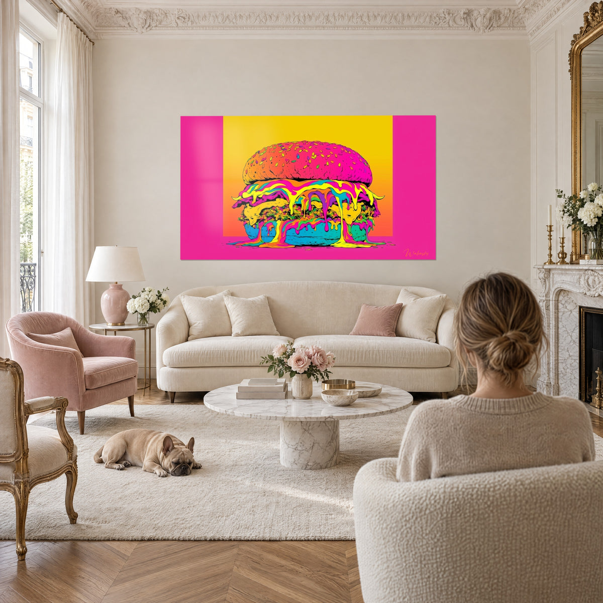 Obraz przedstawiający gigantyczny hamburger z fluorescencyjnymi sosami spływającymi po nim, w fuksjowym różu i słonecznej żółci, naprzeciw kobiety stojącej tyłem, nad sofą w jasnym salonie