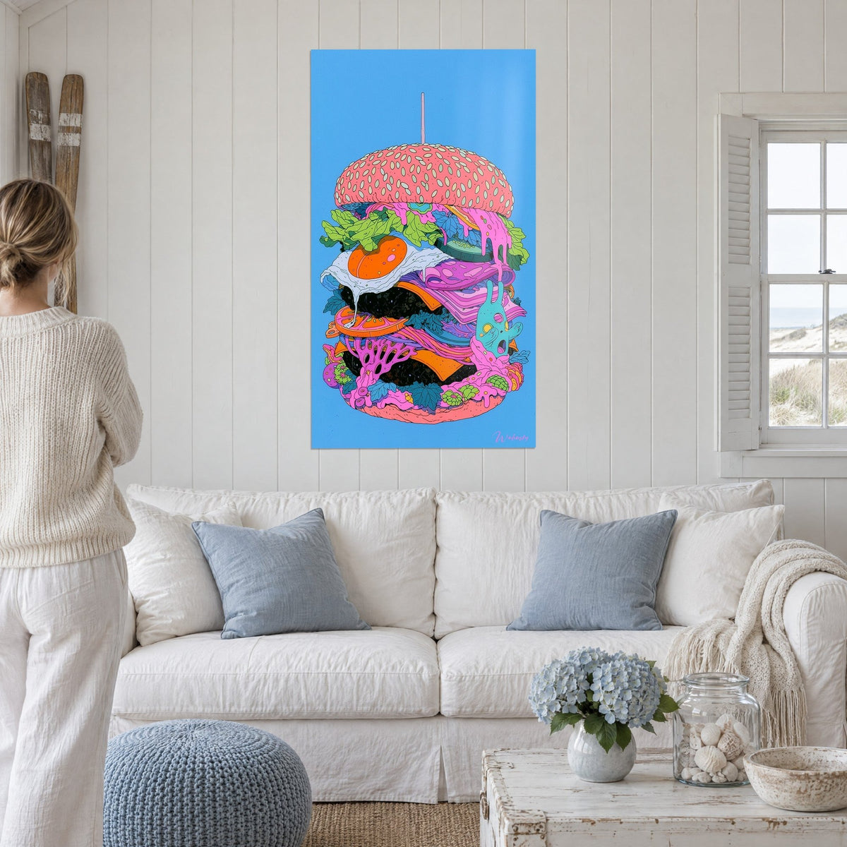 Quadro hamburger gigante con semi di sesamo rosa, uovo arancione e formaggio viola, sopra un divano in un soggiorno luminoso