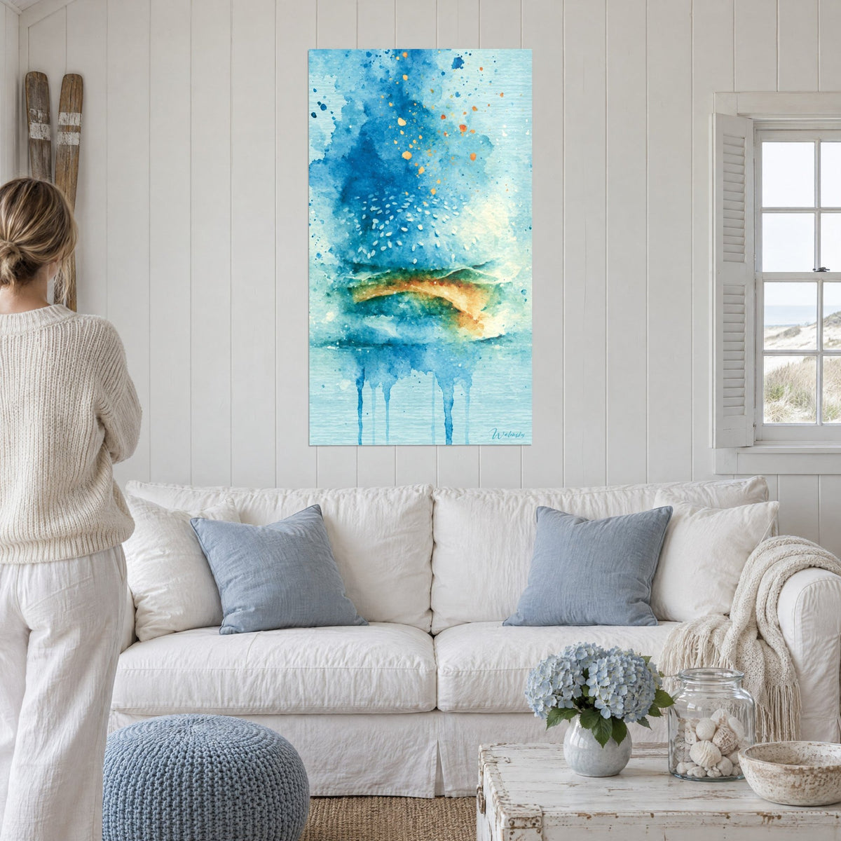 Cuadro hamburguesa en acuarela azul cobalto y ocre dorado, goteos turquesa, una mujer de espaldas sobre un sofá en un salón luminoso