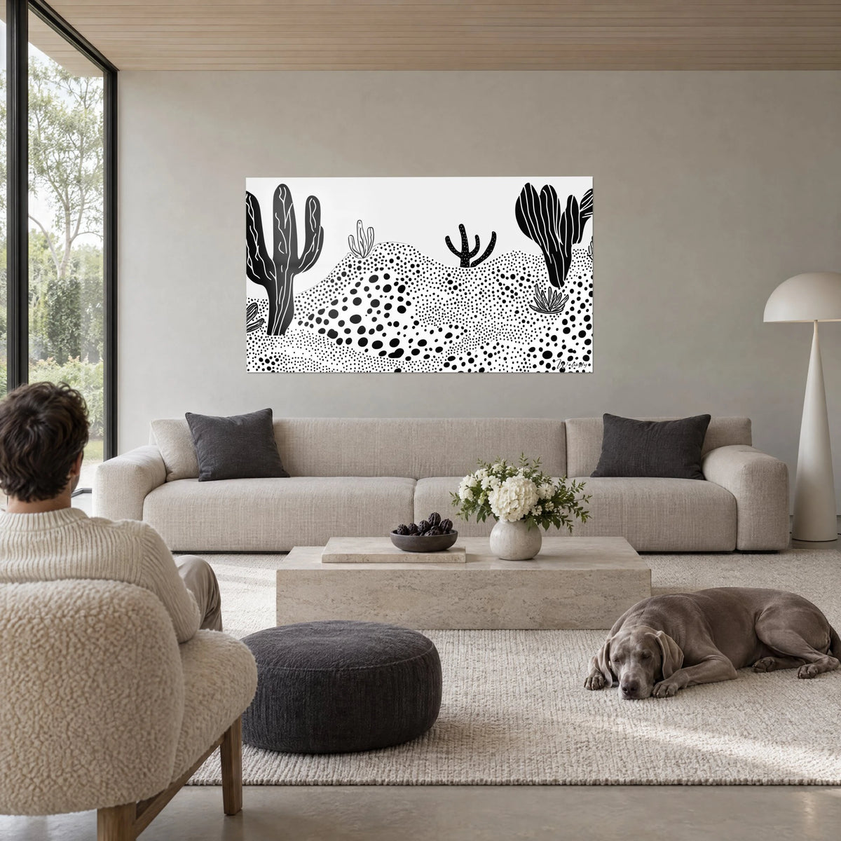 Wall art with giant black cacti and white dotted dunes, a reclining Weimaraner, above a sofa in a bright living room