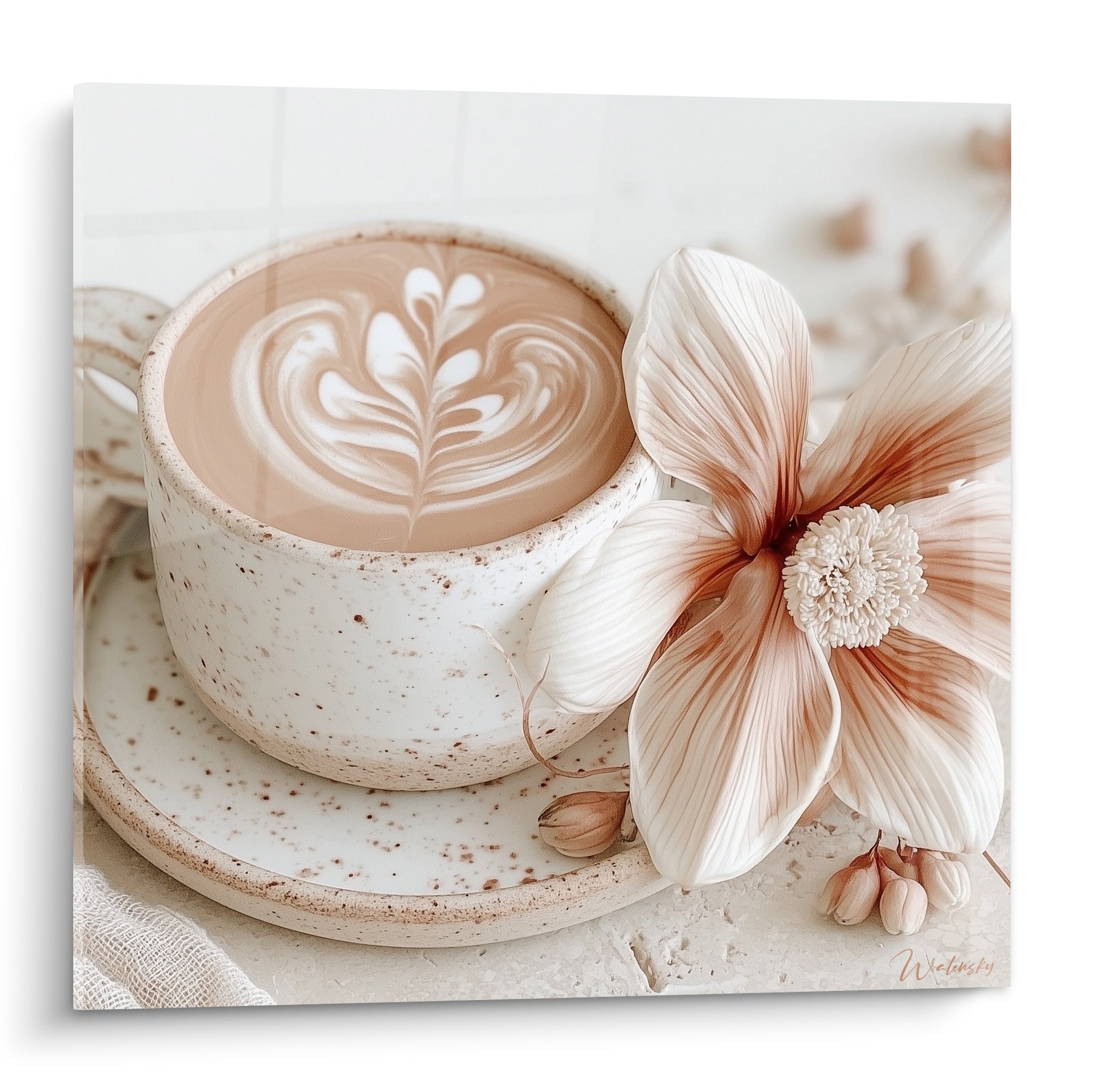 Cappuccino en rosace crème dans une tasse blanche mouchetée, près d'une fleur ivoire veinée de brun