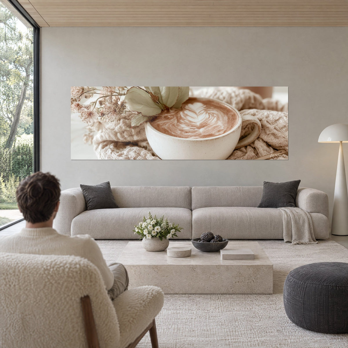 Tableau cappuccino crémeux orné d'une feuille de latte art, brun cacao et blanc cassé, homme de dos au-dessus d'un canapé dans un salon lumineux