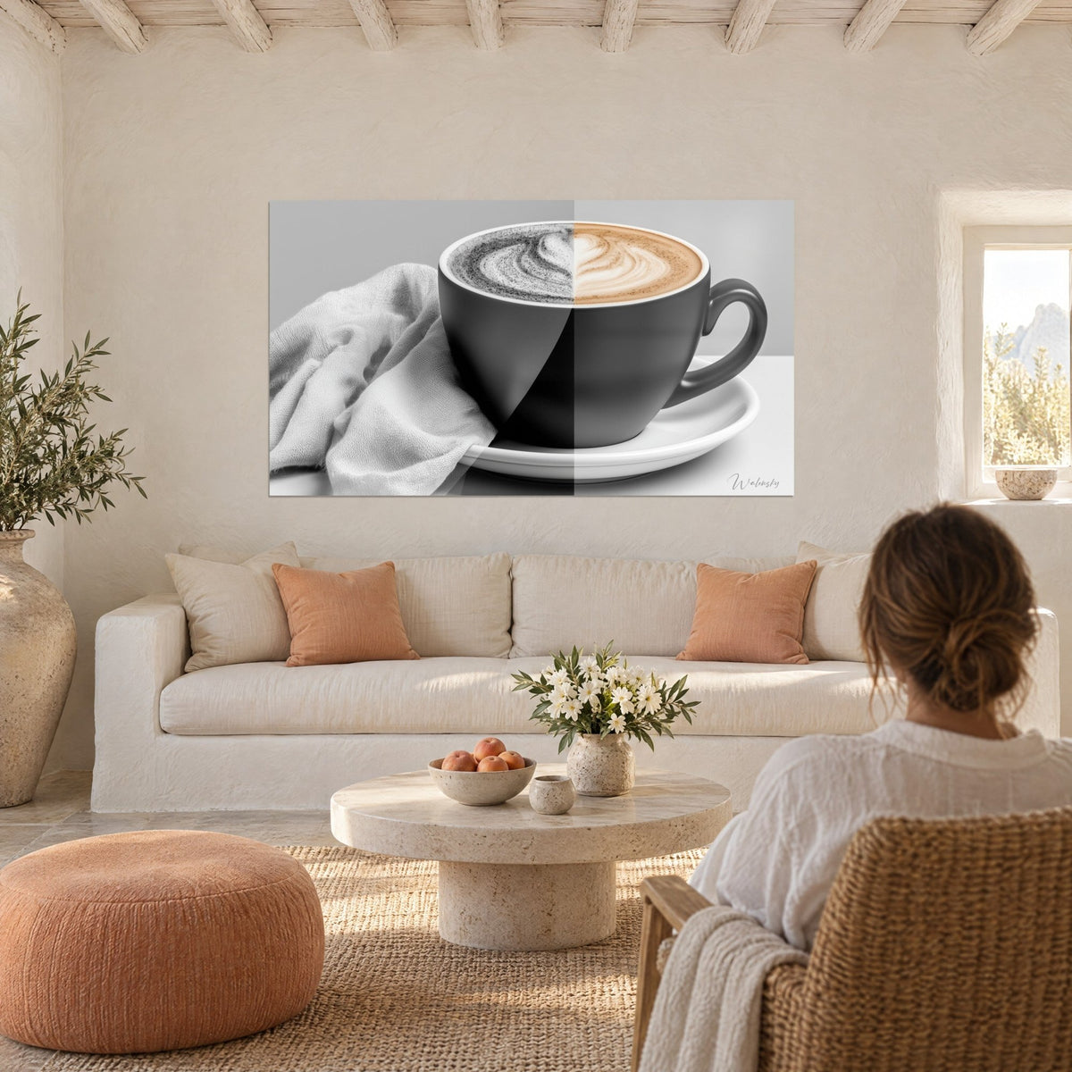 Schilderij latte art tweekleurig in zwart-wit en crèmebruin, zwarte kop op grijs tafelkleed, boven een bank in een lichte woonkamer