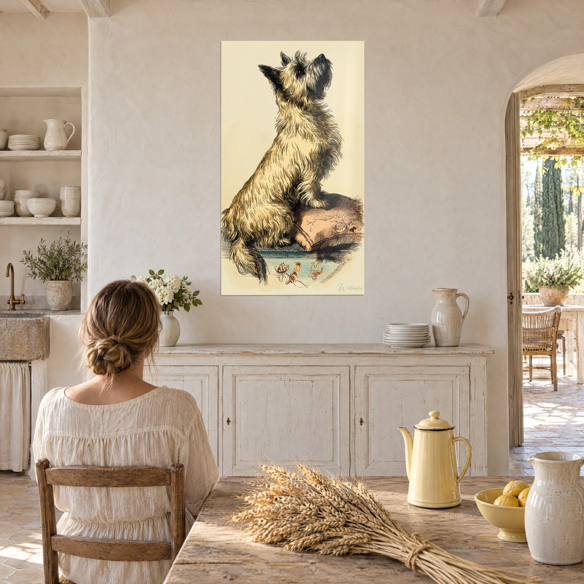 Cuadro grabado vintage de un terrier de perfil, pelaje arena y marrón, orejas erguidas; mujer de espaldas en su mesa de cocina rústica
