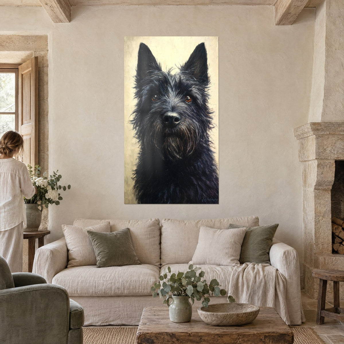 Wall art of a black terrier with amber eyes on an ivory background, tousled fur, woman seen from behind, above a sofa in a bright living room