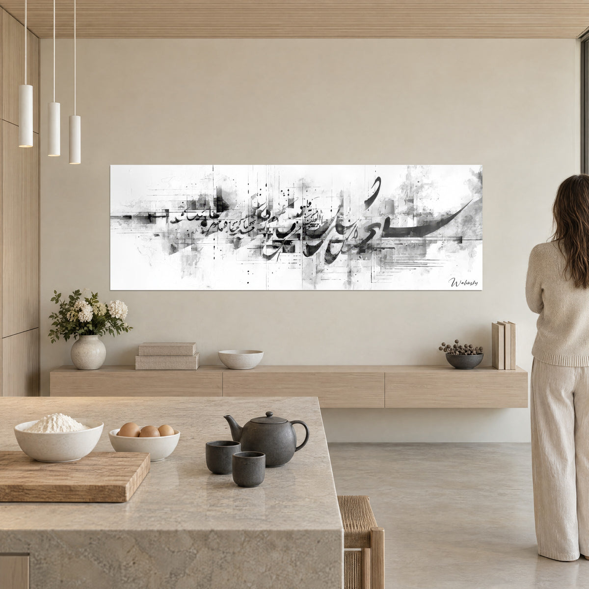 Wall art black calligraphic arabesques, grey and white washes with a skyline feel, a woman seen from behind in an open-plan kitchen