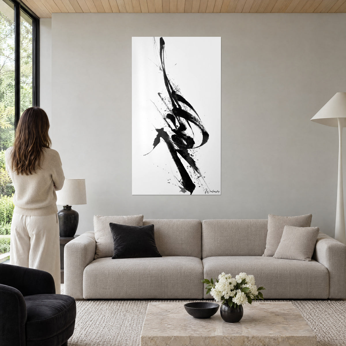 Quadro con gesto calligrafico in bianco e nero, tratti d'inchiostro su fondo avorio, donna di spalle, sopra un divano in un soggiorno luminoso