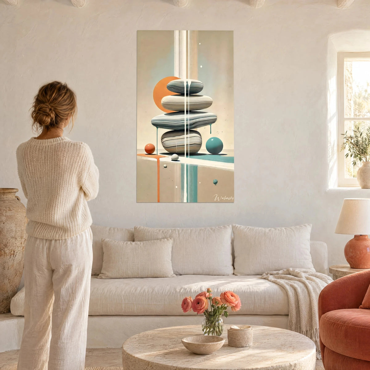 Wall art of stacked stones in balance, orange sun and turquoise sphere, woman seen from behind above a sofa in a bright living room