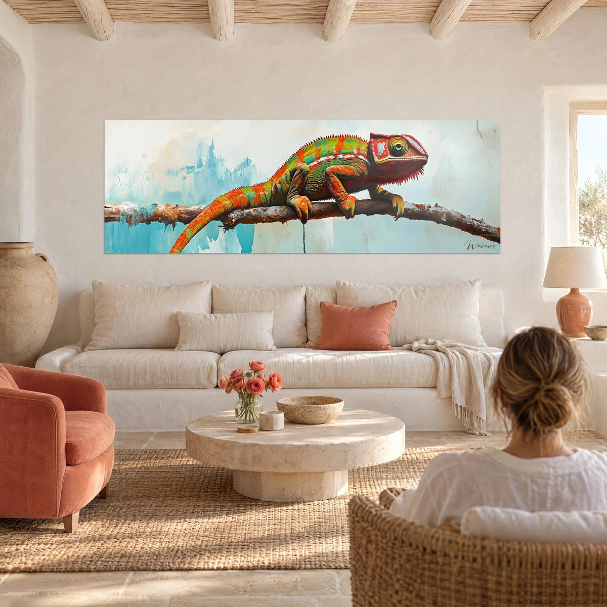 Tableau caméléon orange et vert perché sur une branche, fond turquoise peint, femme de dos au-dessus d'un canapé dans un salon lumineux
