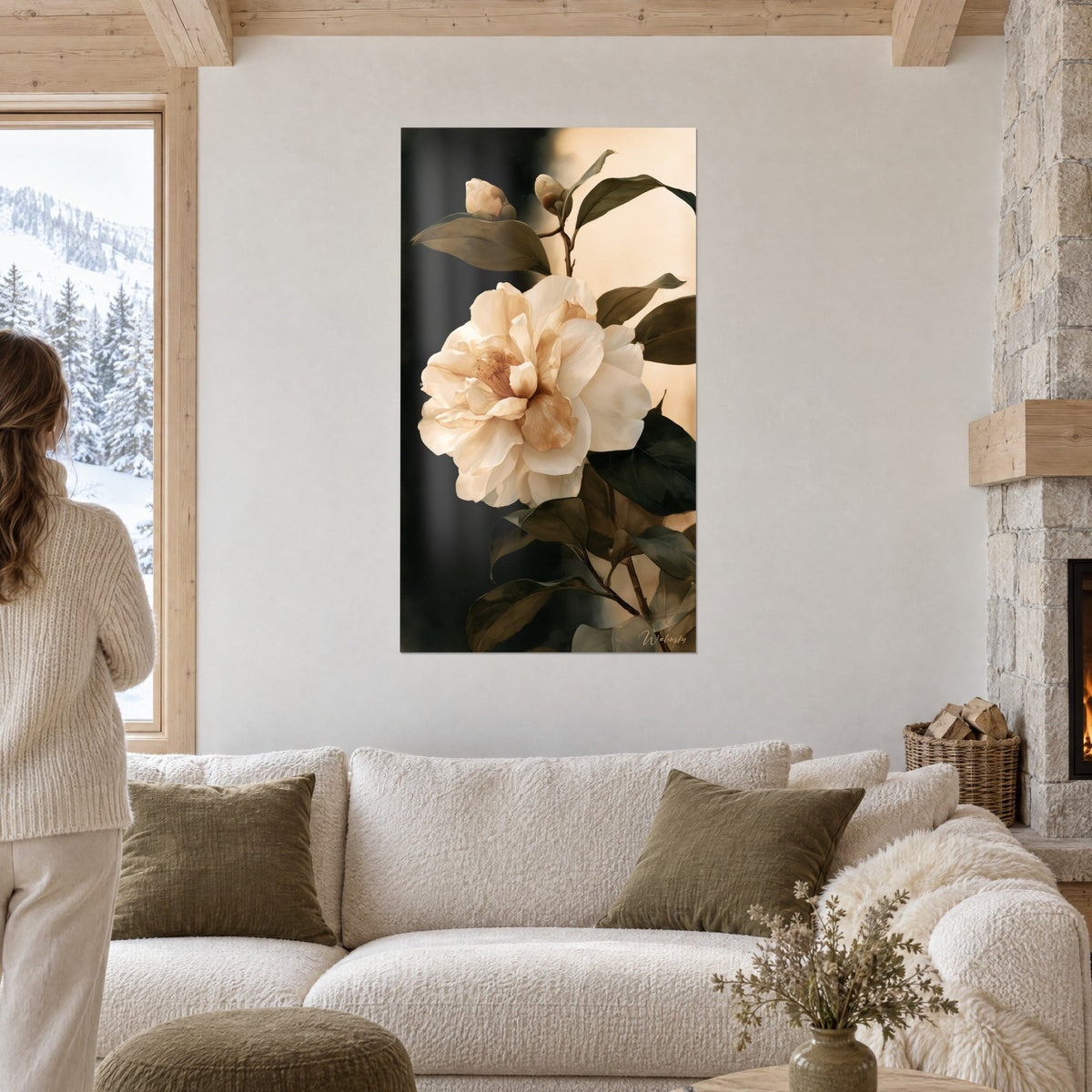 Cuadro camelia crema de pétalos arrugados, follaje verde oscuro sobre fondo negro y arena, encima de un sofá en un salón luminoso