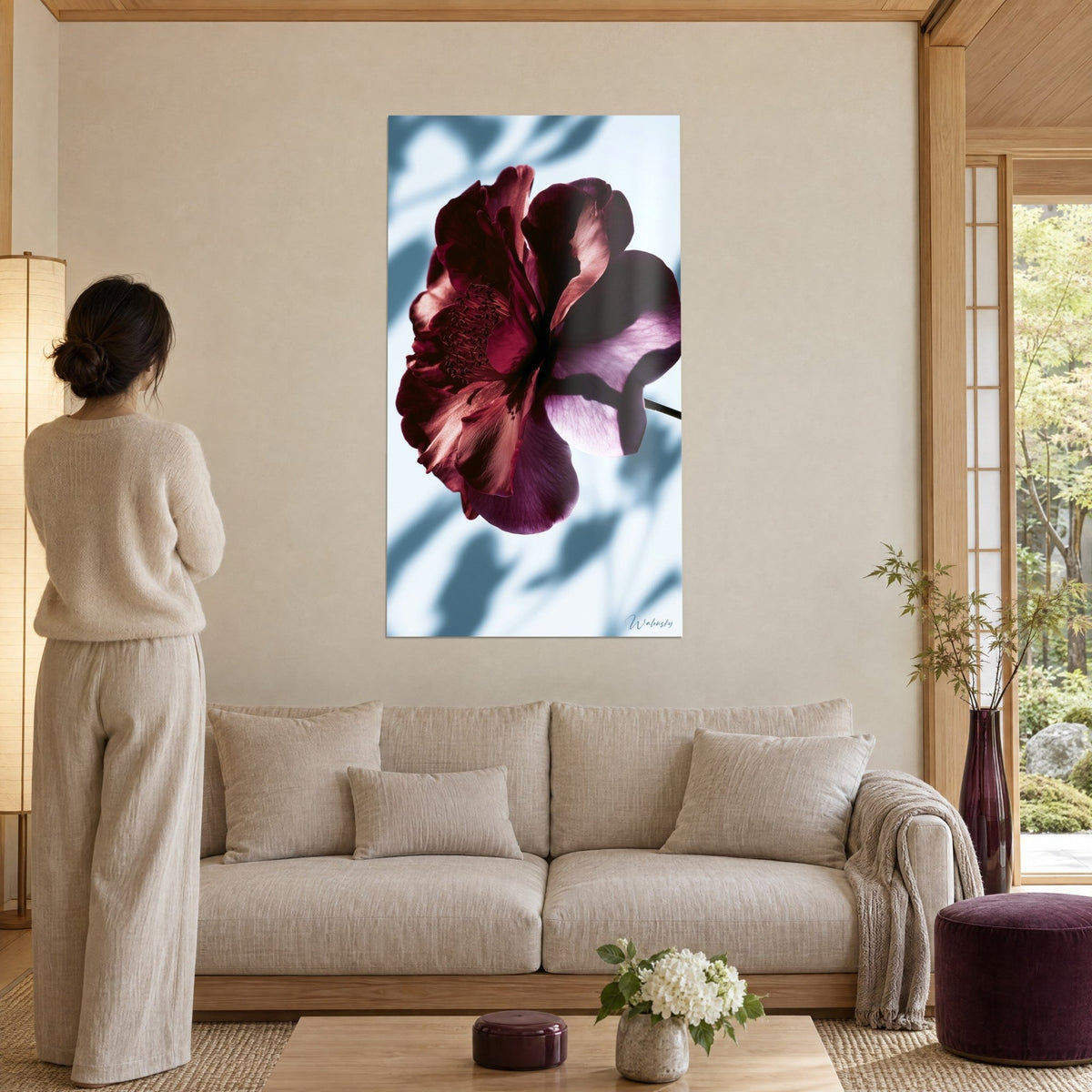 Cuadro camelia púrpura de pétalos burdeos y sombras de hojas azul grisáceo, visto de espaldas sobre un sofá en un salón luminoso