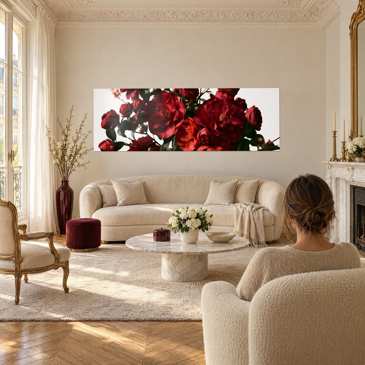 Tableau camélias rouges en grappe aux étamines dorées, feuillage vert sombre, fond ivoire, au-dessus d'un canapé dans un salon lumineux