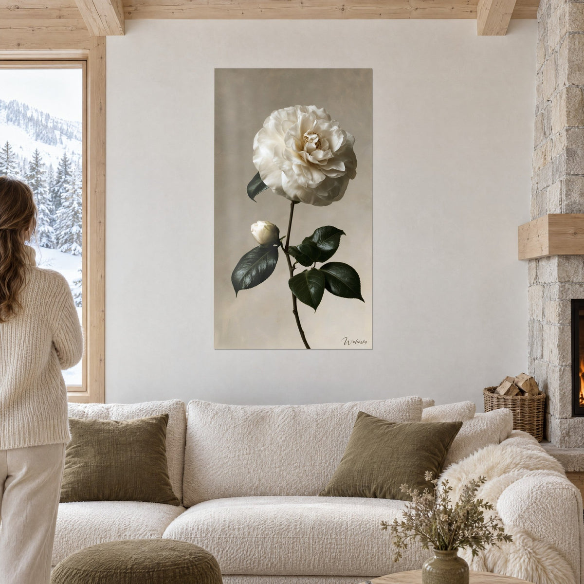 Wall art of a white camellia with crumpled ivory petals and dark green leaves on a beige background, above a sofa in a bright living room
