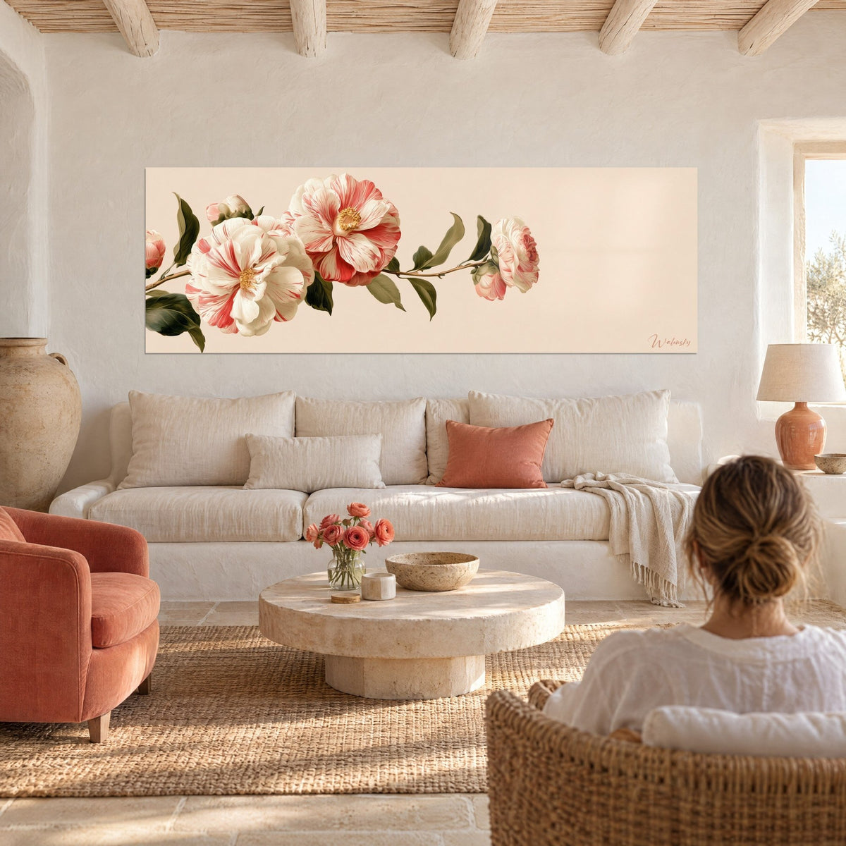 Cuadro de camelias rayadas blancas y coral en una rama larga, fondo rosa pálido, mujer de espaldas, sobre un sofá en un salón luminoso