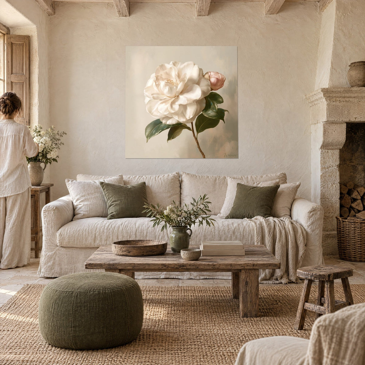 Tableau camélia blanc crémeux et son bouton rose poudré sur fond beige, vu par une femme, au-dessus d'un canapé dans un salon lumineux