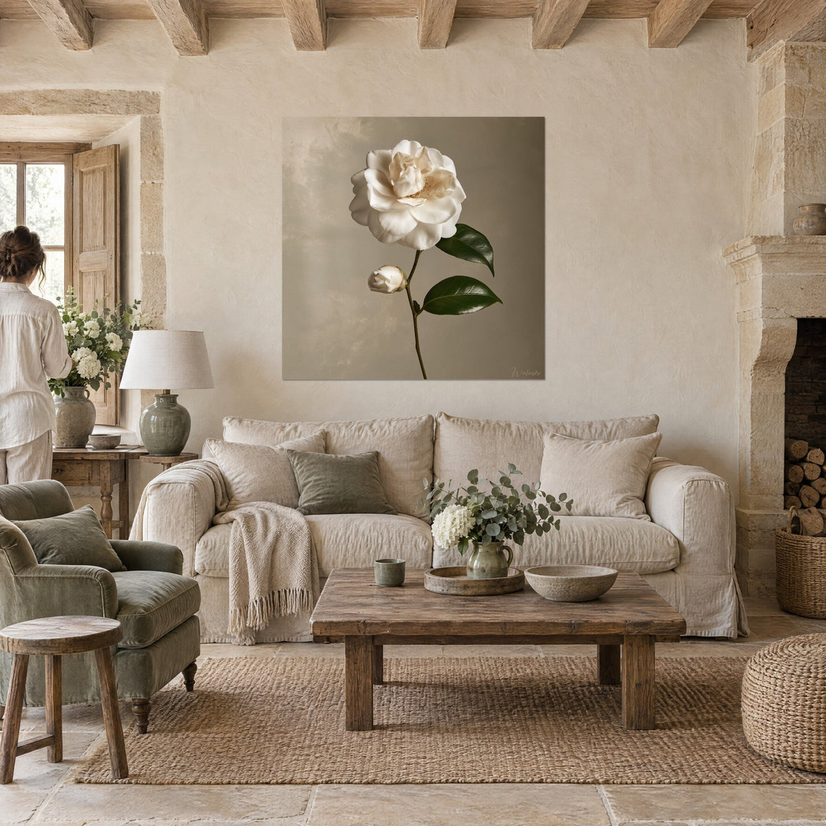 Cuadro camelia blanca con pétalos marfil y hojas verde oscuro, sobre fondo topo, encima de un sofá en un salón luminoso