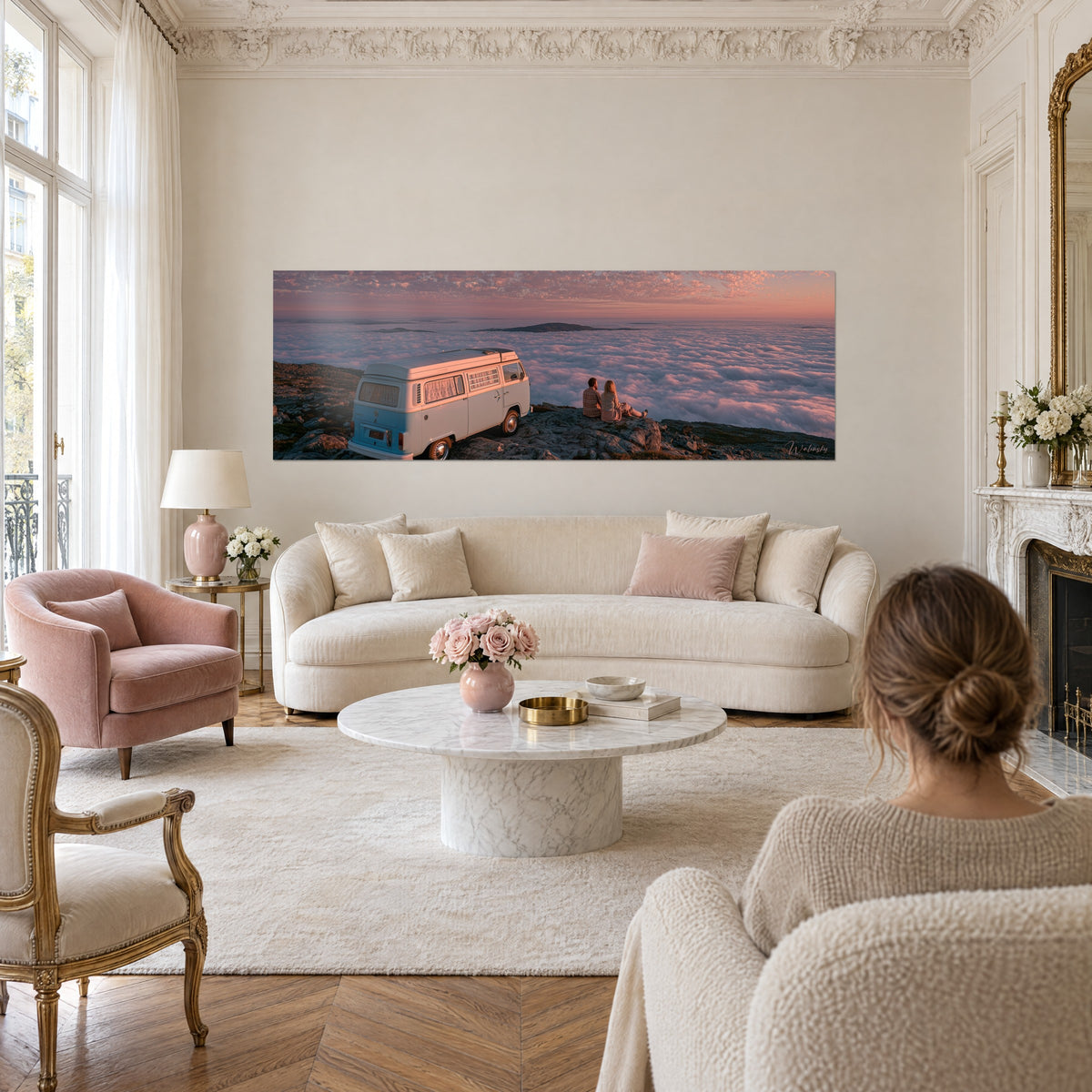 Schilderij in hemelsblauw en crèmewit voor een roze wolkenzee, een stel zittend op de rotsrand, boven een bank in een lichte woonkamer