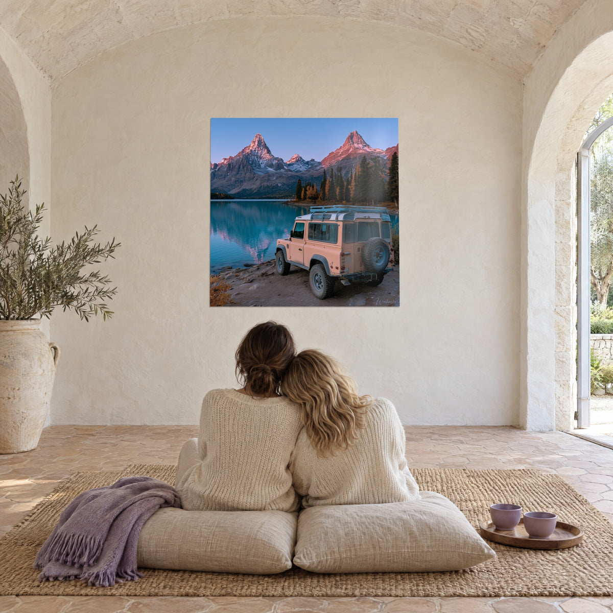 Schilderij roze vintage jeep gekampeerd voor twee vlammende toppen en een turquoise meer, bewonderd door een omhelsd koppel van achteren op kussens