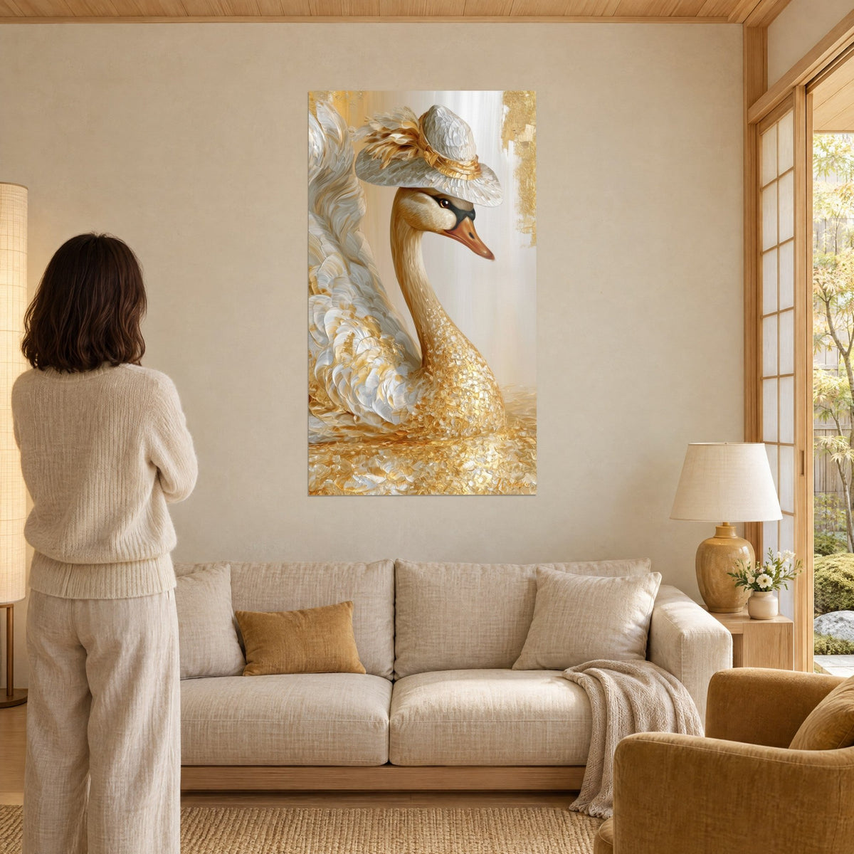 Tableau cygne au chapeau de paille, plumes ivoire et or en relief, mur beige, femme de dos, au-dessus d'un canapé dans un salon lumineux