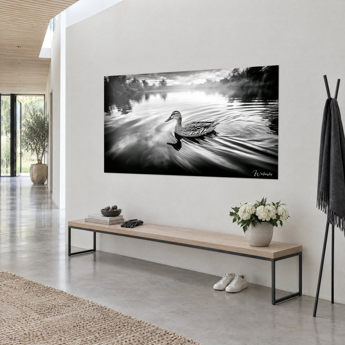Quadro anatra con piume maculate grigio perla e antracite, riflesso scuro sull'acqua, parete bianca e panca in rovere chiaro