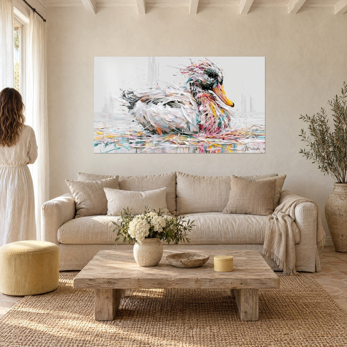 Tableau canard blanc au bec doré éclaboussé de rose et turquoise, une femme de dos, au-dessus d'un canapé dans un salon lumineux