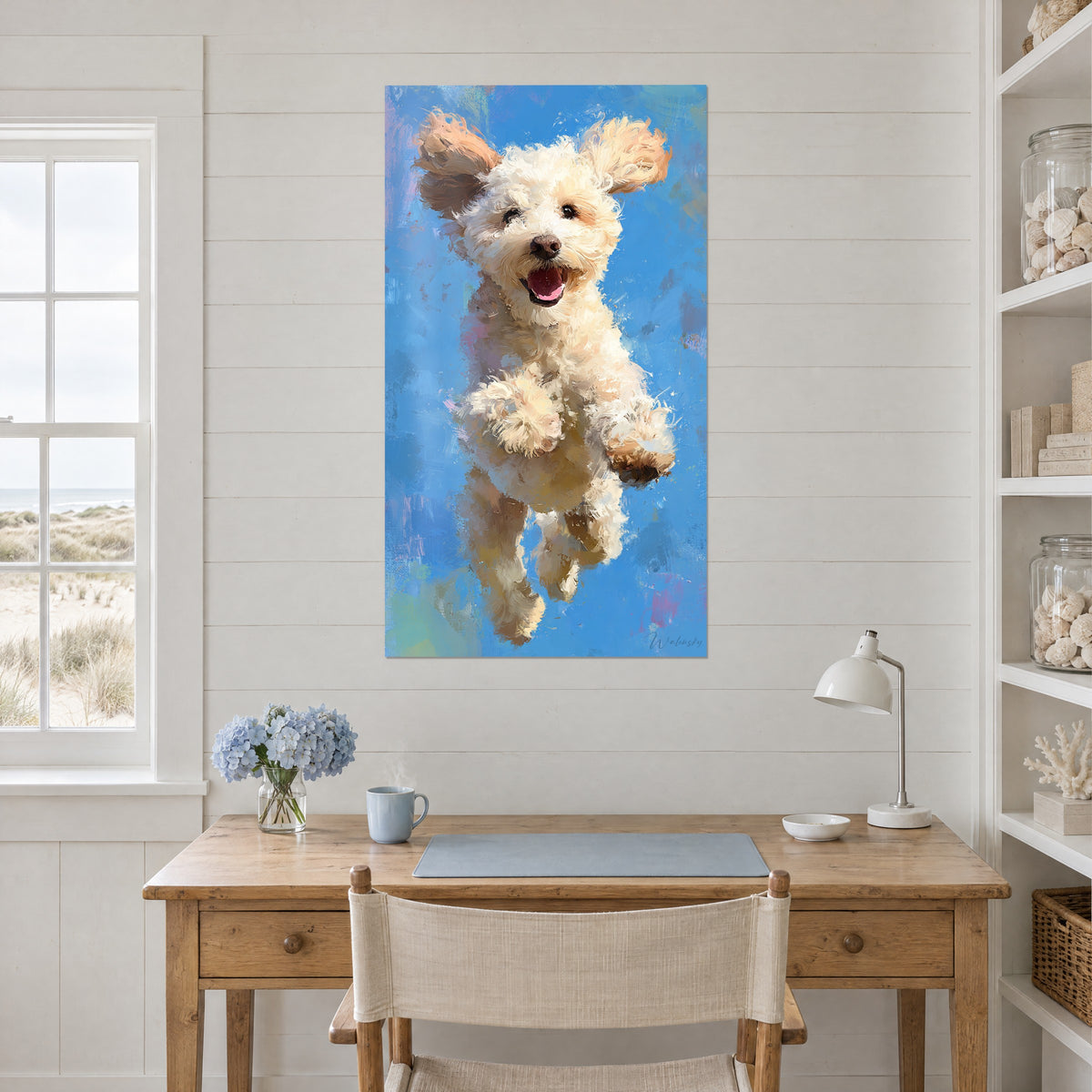 Cuadro perro rizado color crema saltando sobre fondo turquesa, colgado encima de un escritorio de madera clara