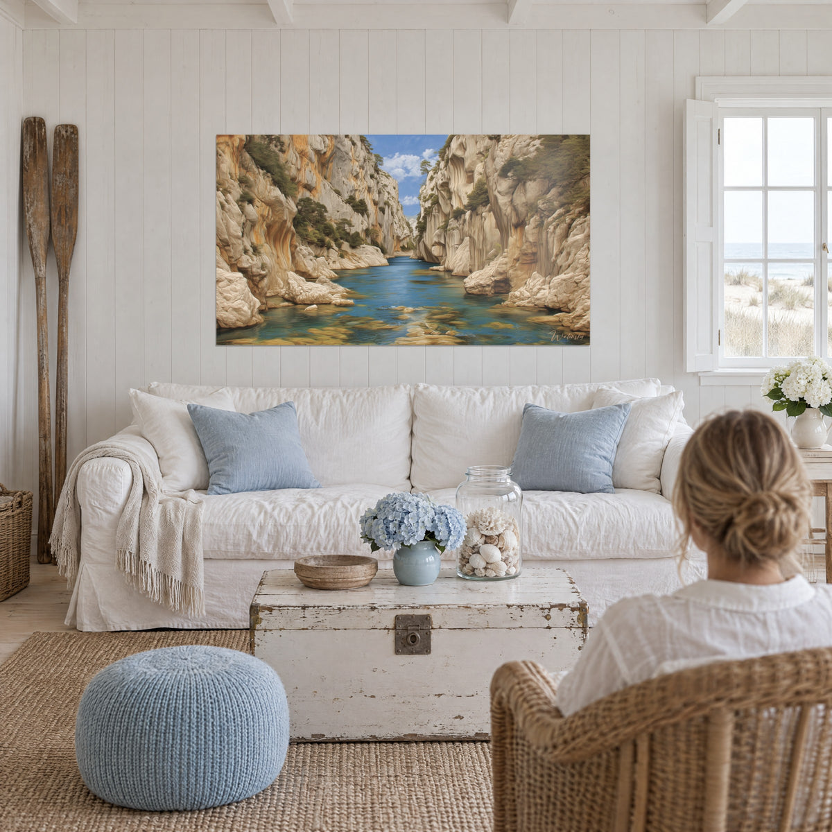 Wall art canyon with cream limestone walls and turquoise water, green pines, woman seen from behind, above a sofa in a bright living room
