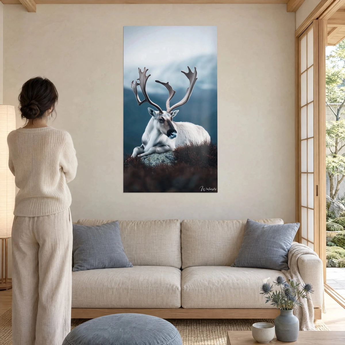 Wall art white reindeer lying in the heather, brown antlers, bluish mountain, above a sofa in a bright living room