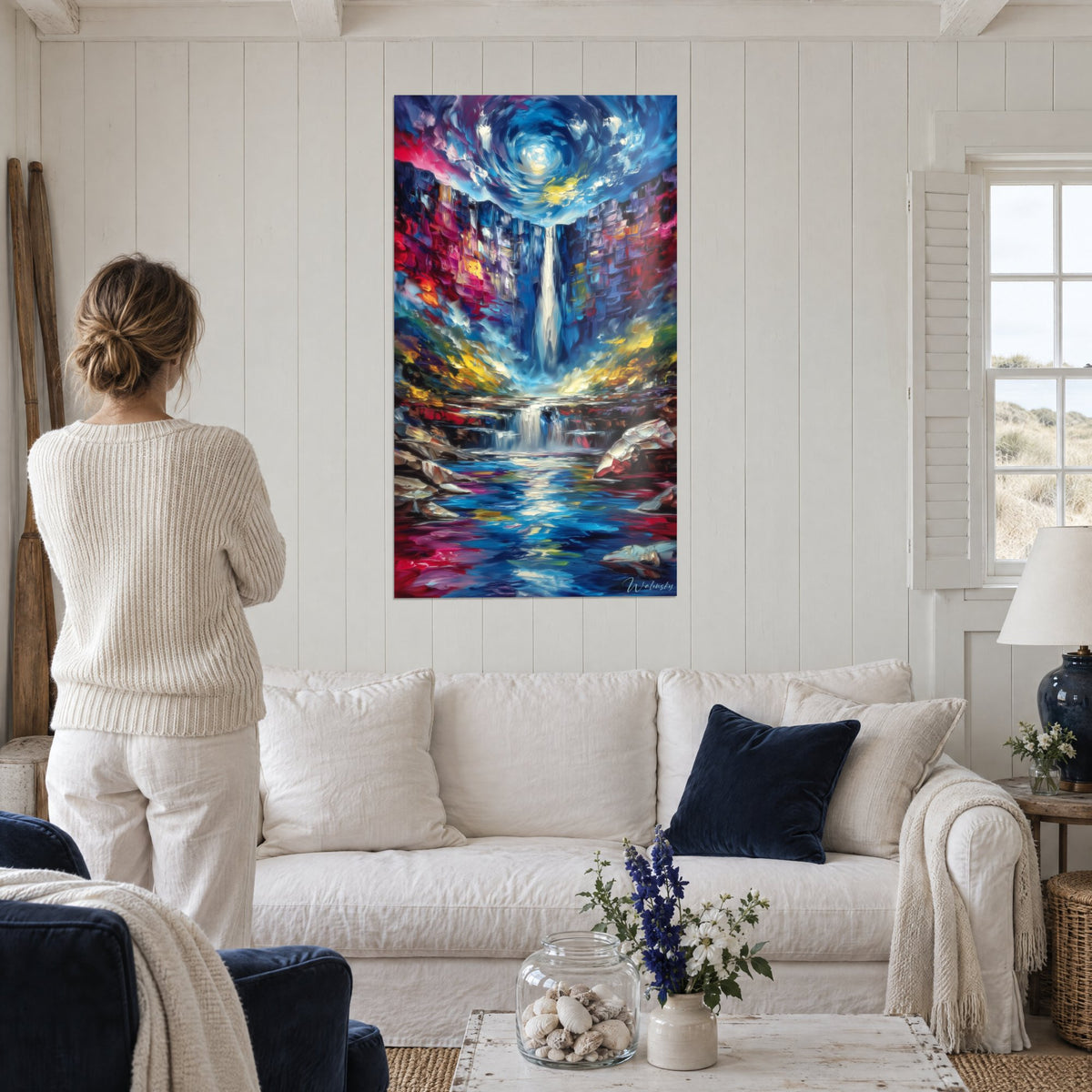 Wall art waterfall cutting through a red and purple canyon under a swirling blue sky, above a sofa in a bright living room