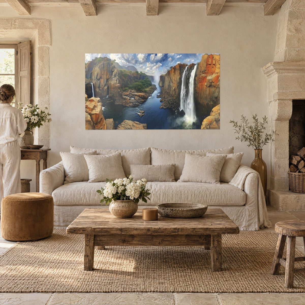 Wall art canyon with orange cliffs and a white waterfall over a midnight-blue river, a woman seen from behind, above a sofa in a bright living room