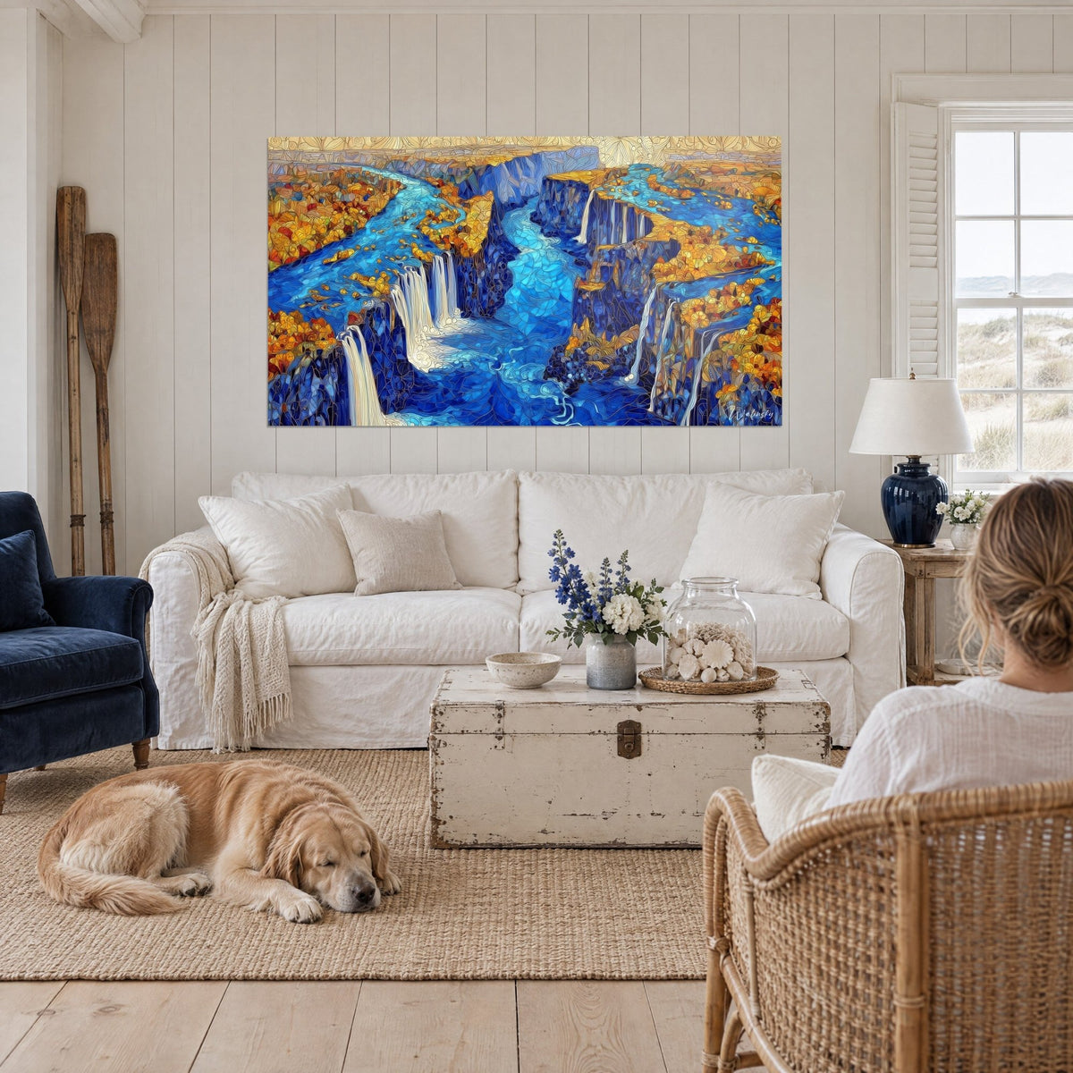Gemälde Canyon mit Kaskaden in Kobaltblau und ockerfarbenem Laub, Frau von hinten und Retriever, über einem Sofa in einem hellen Wohnzimmer